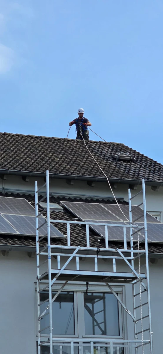 Technicien sur toit équipé de panneaux solaires, nettoyant l’installation photovoltaïque avec échafaudage et harnais