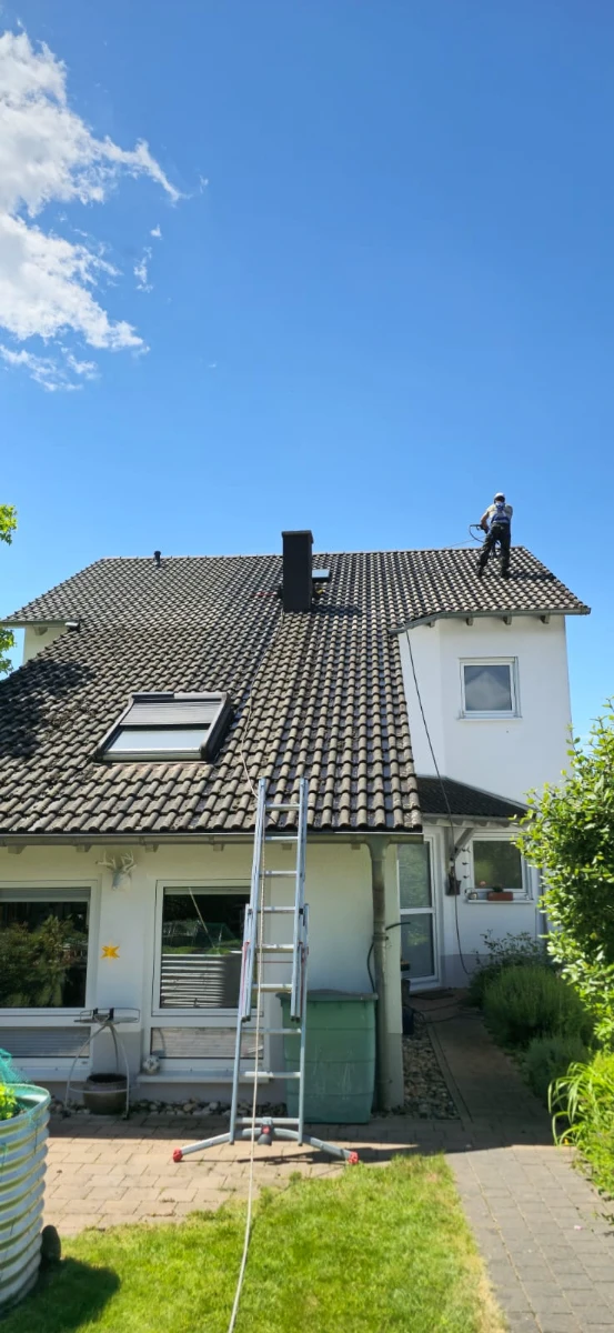 Nettoyage du toit d’une maison par un technicien sur une échelle sous un ciel bleu