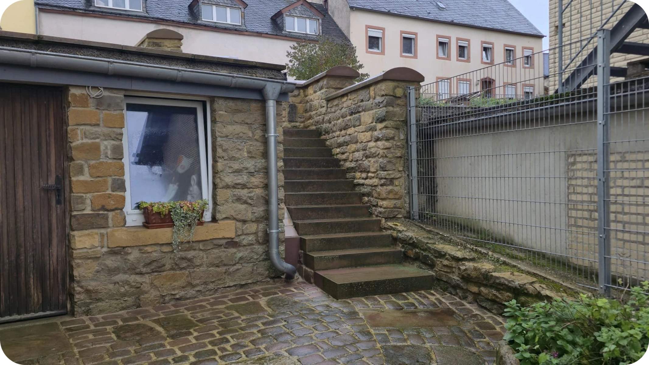 Cour pavée humide devant mur en pierre et escalier en pierre, nettoyage de cour